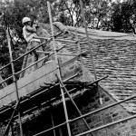 A craftsman up a scaffold tower working on the roof of a large country cottage.